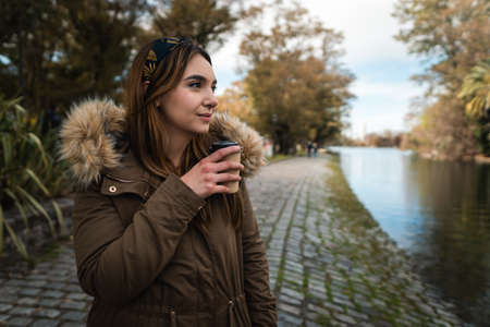 A pretty caucasian woman smiling while holding a coffee and enjoying a walk at park. Copy spaceの写真素材