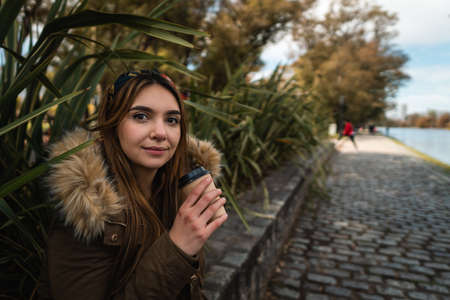 A pretty woman smiling at camera while relaxing at park and drinking a coffee. Verticalの写真素材