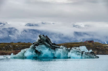 Black iceberg with typical greenland houses and mountains behind