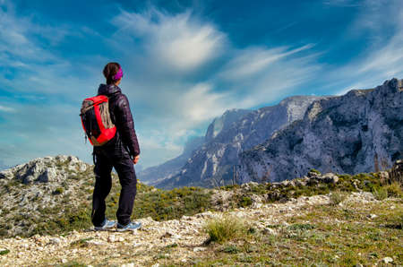 A girl with a backpack beholding the landscape in te top of a hill. Blue sky with cloudsの写真素材