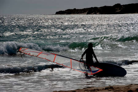 Image of a windsurfer in silhouette going out if the beachの写真素材