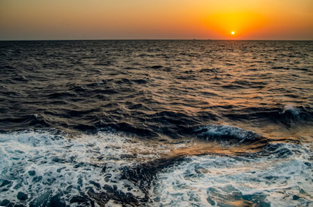 Beautiful sunrise / sunset in an orange sea with a wave splashing in the foregroundの写真素材