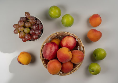 top view of fruits as nectarines and pluots in basket with grapes in bowl and green pluots on white...