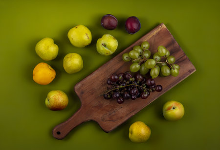 top view of grapes on cutting board with pattern of pluots and nectacot on green backgroundの写真素材