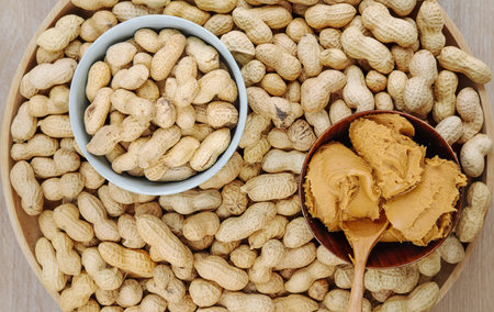 top view of peanut butter in a wooden bowl with a bowl filled with peanuts on wooden background