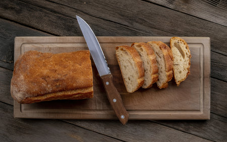 top view of sliced crusty bread and knife on cutting board on wooden background