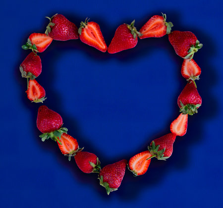 top view of strawberries on blue background with copy space heart conceptの写真素材