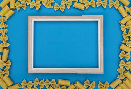 top view of macaronis as farfalle fusilli penne pipe-rigate around frame on blue background with copy spaceの写真素材