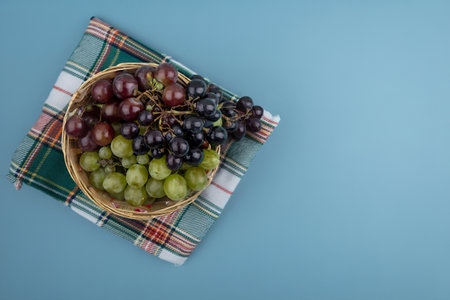 top view of grapes in basket on plaid cloth on blue background with copy spaceの写真素材