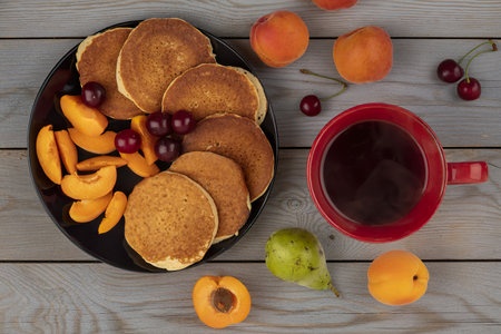 top view of pancakes with cherries and sliced apricot in plate and cup of coffeeの写真素材