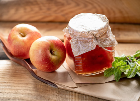 One full small glass jar closed with homemade paper lid with homemade apple jam and two whole applesの写真素材
