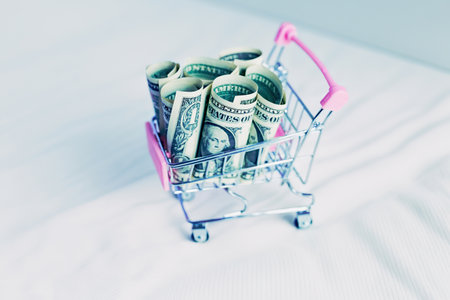miniature shopping cart filled with one dollar banknotes on white background