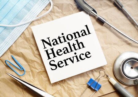 Text NHS National Health Service on white sticker and stethoscope, blue mask and penの写真素材