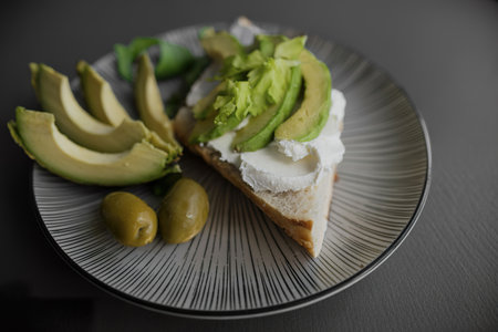 Healthy avocado toast serves on a modern patterned plate with olivesの素材