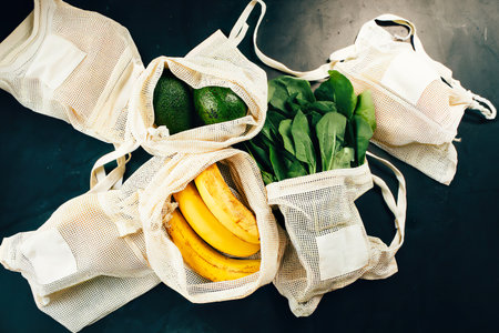 Avocado, bananas and spinach in eco cotton bags on table. Zero waste shopping concept