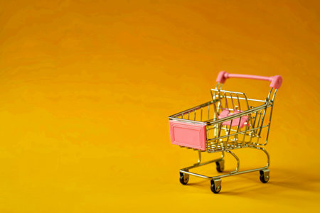 empty pink miniature shopping cart on yellow backgroundの写真素材