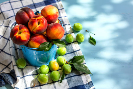 top view of fresh juicy peaches on a bucket with green cherry plums on a checked tableclothの写真素材