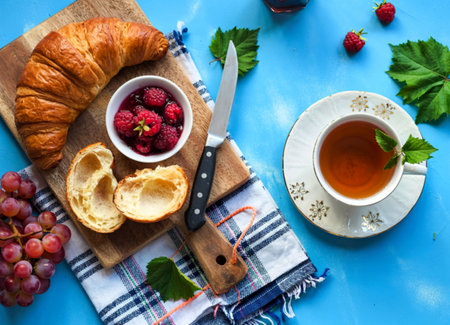 top view of croissant and raspberry jam in bowl grape with knife on cutting board on plaid clothの写真素材
