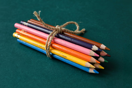 side view of colored pencils tied with a rope on dark green backgroundの写真素材