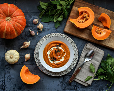 A fresh pumpkin is sliced into pieces on a kitchen cutting board and a plate with pumpkin soupの写真素材