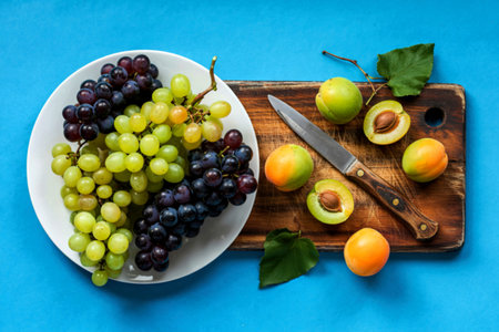 top view of black and white grapes in plate and green pluots apricots with knifeの写真素材