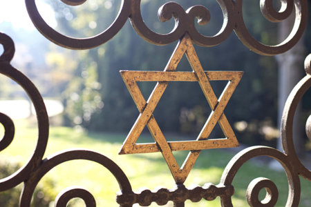 A close-up view of an ornate metal gate featuring a prominent gold Star of David, set against a...