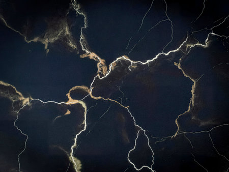 A high-resolution image showcasing a dark marble texture with prominent white and beige veining creating a striking contrast. The pattern resembles lightning strikes across a dark sky.の写真素材