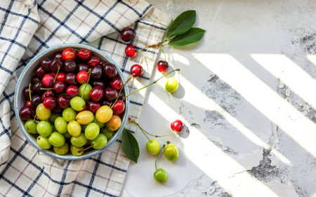 top view of fresh fruits such as cherriessloes and green cherry plums on a bowl on a checked tableclothの写真素材