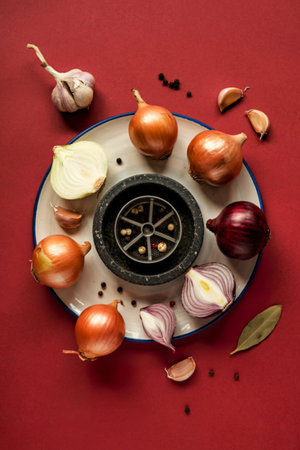 top view of different whole and sliced onions and black pepper in garlic crusher around plateの写真素材
