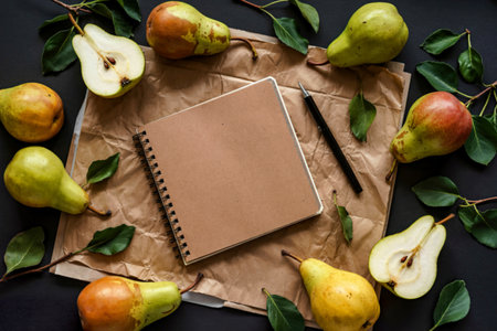 top view of sketchbook made of craft paper framed with fresh ripe pears on black background