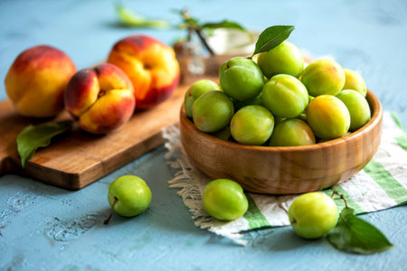 side view of green plums on a wooden bowl with yellow peaches isolated on a wooden kitchen boardの写真素材