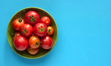 top view of tomatoes in bowl on left side and blue background with copy spaceの写真素材