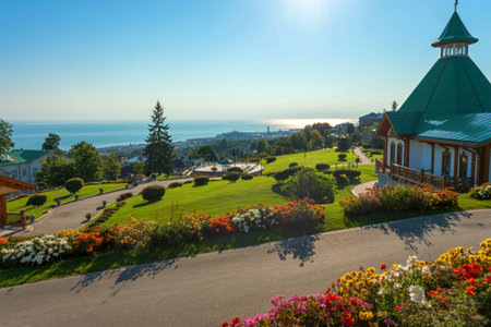 A picturesque scene showcasing a beautifully landscaped hilltop garden overlooking a calm ocean. A charming gazebo with a green roof is a focal point.の写真素材