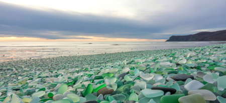 A stunning beach covered in smooth, sea-worn glass pieces in shades of green and white, stretches...