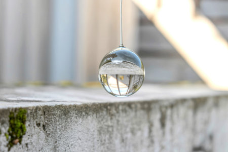 A clear glass sphere hangs suspended, reflecting a blurred image of a light-colored building and its...