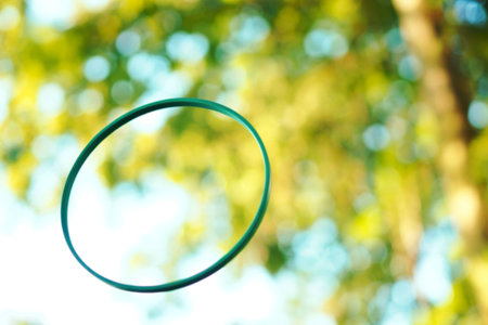 A vibrant teal ring is suspended in the air, set against a softly blurred backdrop of green foliage...