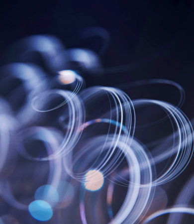 An abstract image featuring blurred, swirling light trails in shades of white and blue against a dark background. The composition creates a sense of movement and energy.の素材