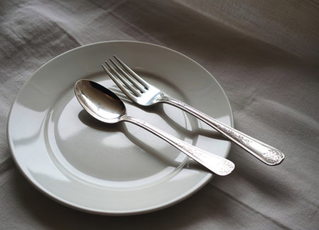 A simple yet elegant scene featuring a silver spoon and fork delicately placed on a pristine white...