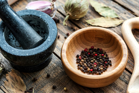 Closeup black pepper in wooden bowl with mortar and pestle on shabby teak wood table