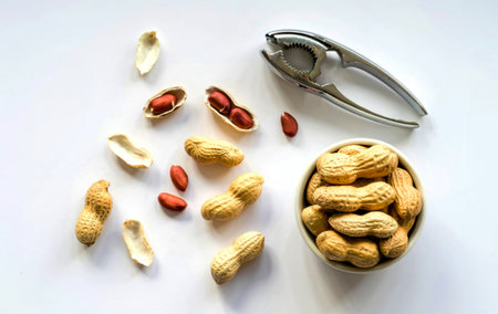 top view of peanuts in a bowl with nut cracker on white background