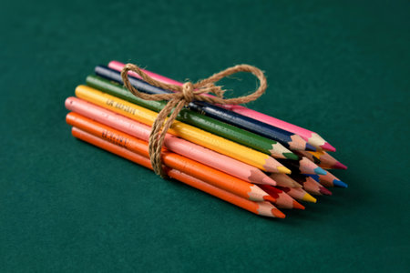 side view of colored pencils tied with a rope on dark green background