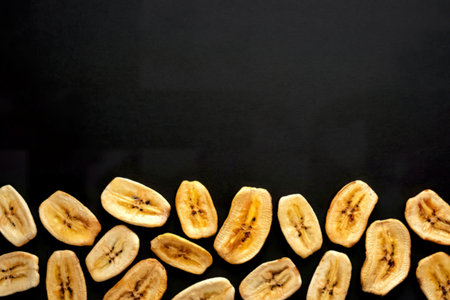 top view of dried banana chips arranged at the bottom on black background with copy space