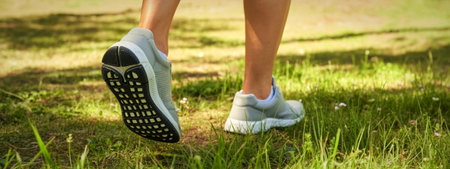 Close-up view of a woman's legs and feet wearing light gray running shoes while walking or jogging...