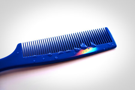 A vibrant blue comb lies on a white surface, its teeth glistening with water droplets. Light refracts through the water, creating subtle rainbow colors.の写真素材