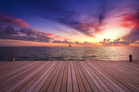 A tranquil ocean scene at sunset, featuring a sailboat on the horizon and a foreground of a wooden...
