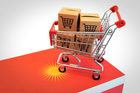 A small metal shopping cart overflows with cardboard boxes, each featuring a shopping cart icon. It rests on a vibrant red surface adorned with a yellow sun symbol.の写真素材