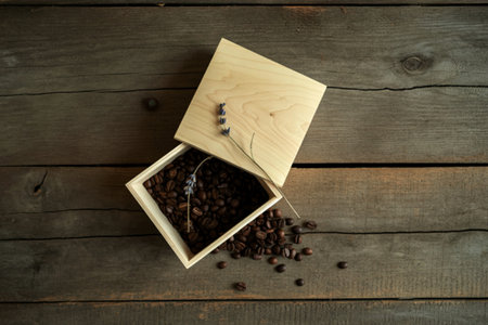 A rustic wooden box overflowing with dark roasted coffee beans and a sprig of lavender rests on a weathered wood surface.の写真素材