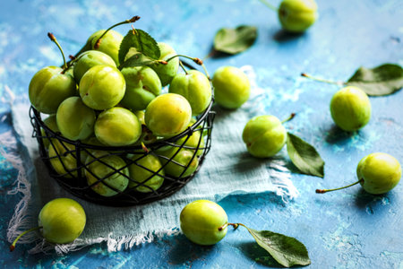 top view of fresh green cherry plums on a black basket on a blue backgroundの写真素材