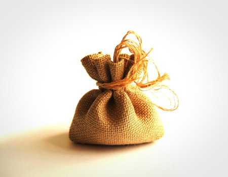 A small, tightly cinched burlap bag with a rough texture sits on a smooth white surface. A frayed twine tie secures the opening, creating a rustic and simple presentation.の写真素材