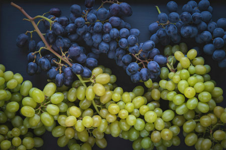 A top-down view showcases two bunches of grapes, one a vibrant green and the other a deep blue,...